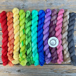 A pastel rainbow of small skeins rests on a wooden background