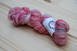 a sparkly skein of yarn in reds, cream, and black rests on a light wooden background. 