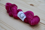 a bright twist of yarn rests against a light wooden background. 