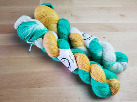 Two bright skeins of yarn rest against a light wooden background.