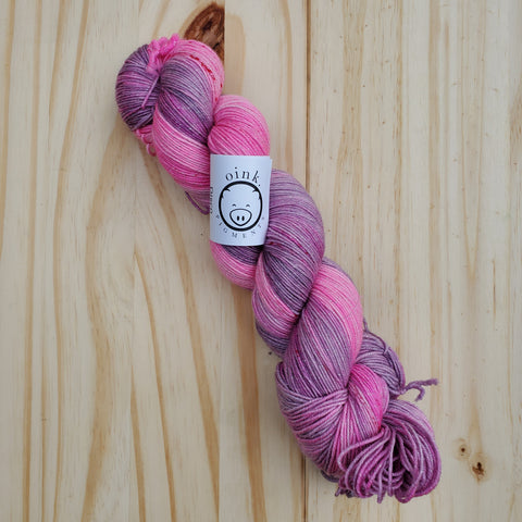A bright skein of pink & purple yarn rests on a light wooden background.