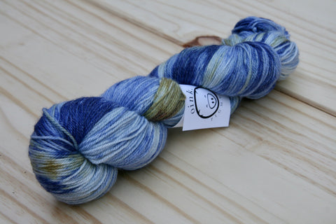 a skein of deep blue with lighter blue and dark gold tones rests on a light wooden background. 