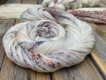 A swirl of yarn rests on a wooden tabletop.  Two other skeins can be seen in the background.