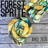 a skein of mustard yellow, light yellow yarn with teal and black speckles sits in a twisted bun stop a wooden background.  Three skeins sit in the upper right corner, and black text reads "forest sprite, April 2020" 